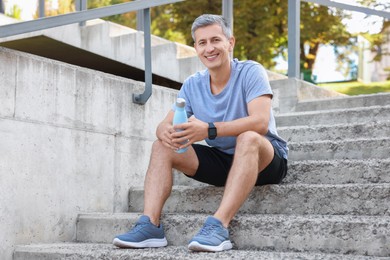 Photo of Smiling man with bottle of water on steps outdoors