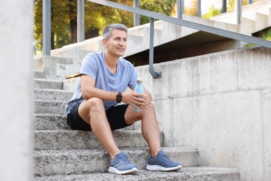 Photo of Smiling man with bottle of water on steps outdoors