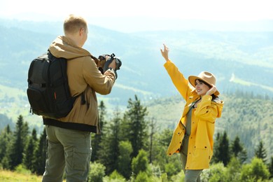 Photo of Photographer with backpack and camera taking picture of model in beautiful mountains