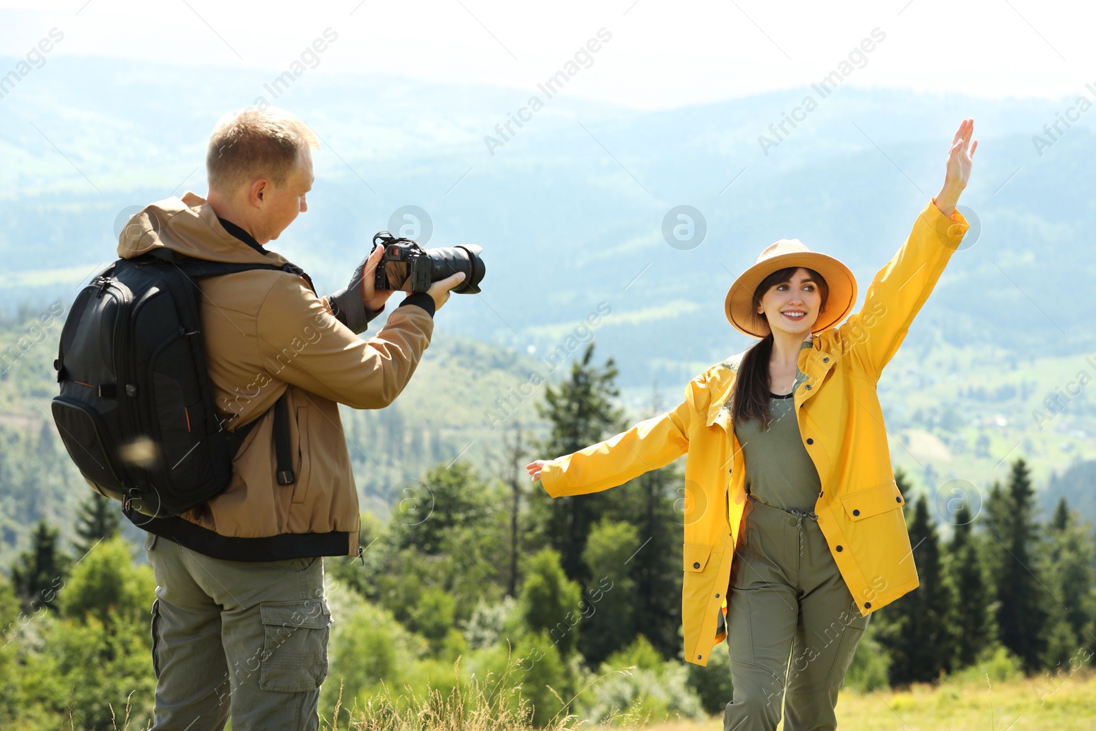 Photo of Photographer with backpack and camera taking picture of model in beautiful mountains