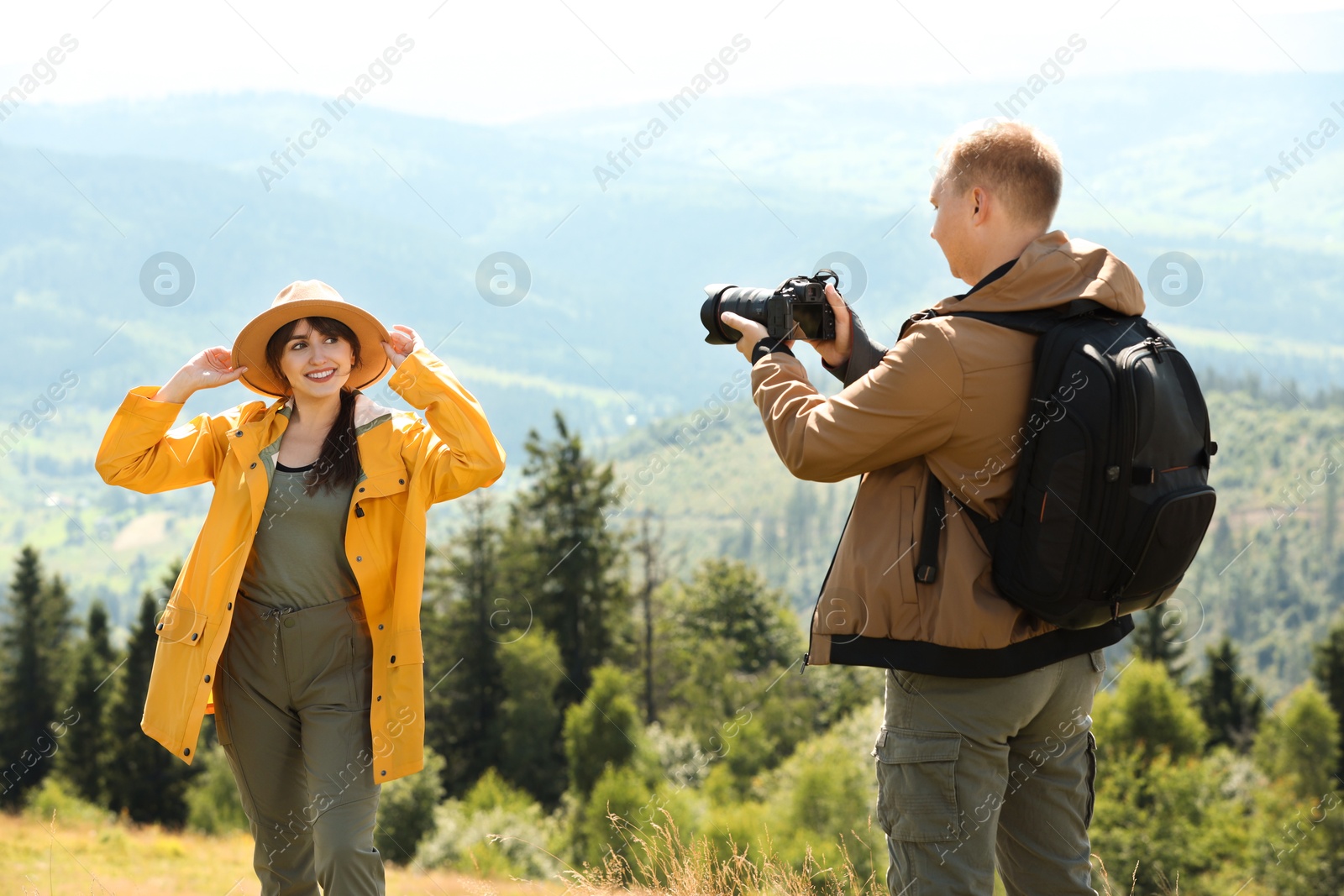 Photo of Photographer with backpack and camera taking picture of model in beautiful mountains