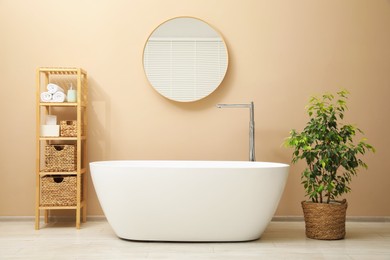 Photo of Bathtub, houseplant, shelving unit and mirror in stylish bathroom