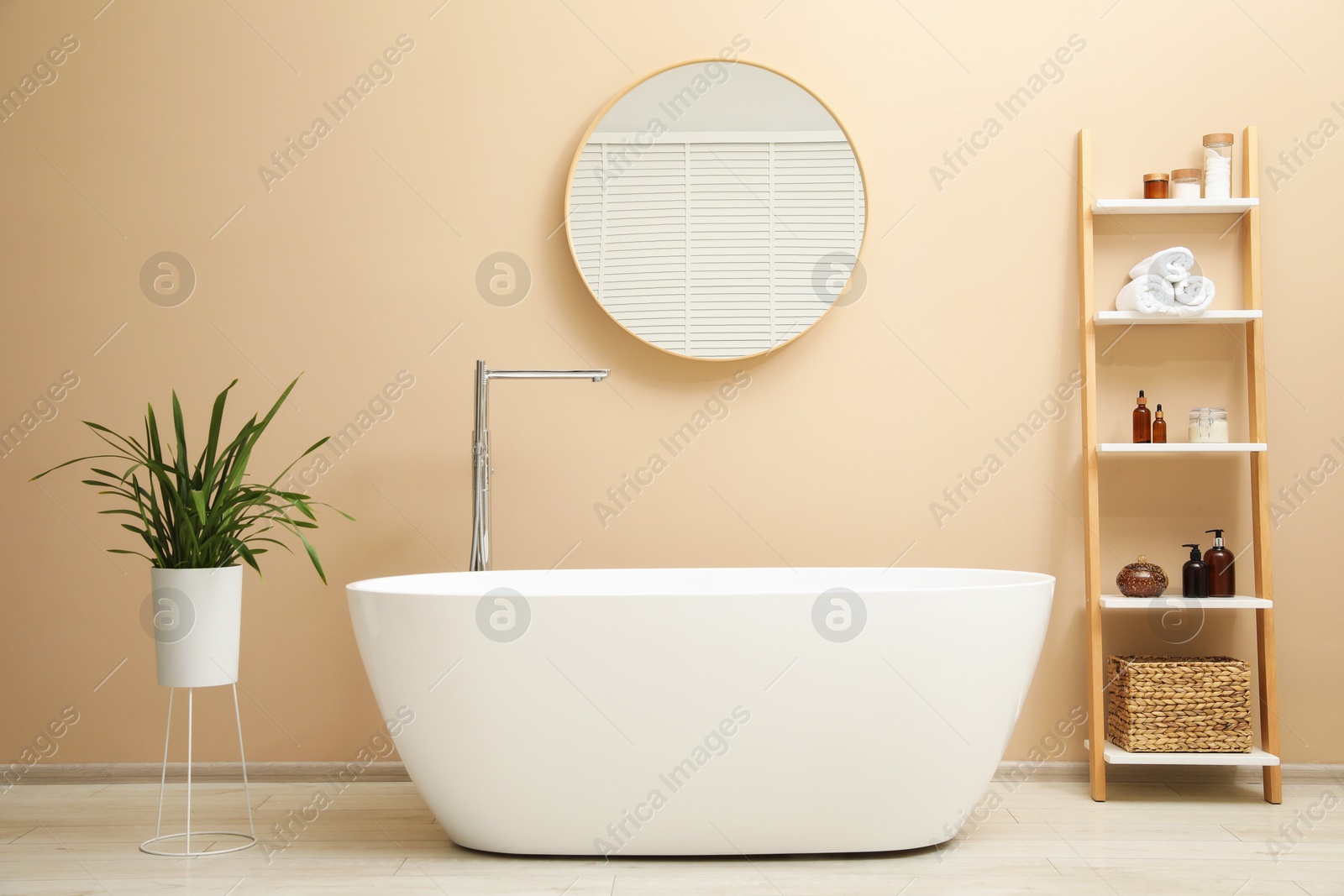 Photo of Bathtub, houseplant, shelving unit and mirror in stylish bathroom