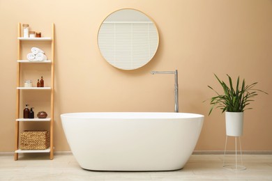 Photo of Bathtub, houseplant, shelving unit and mirror in stylish bathroom