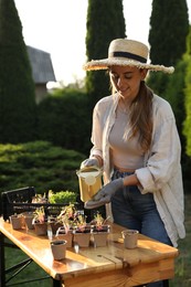 Photo of Smiling woman watering potted seedlings with can at table outdoors