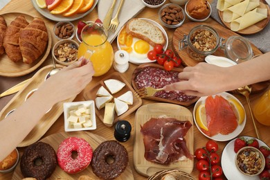 Photo of Women eating different food during brunch at wooden table, top view