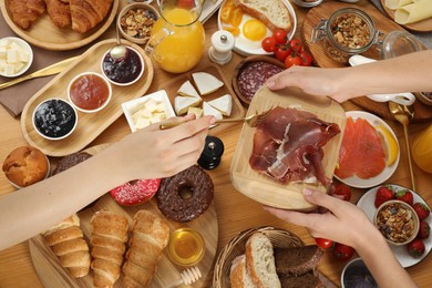 Photo of Women eating different food during brunch at wooden table, top view