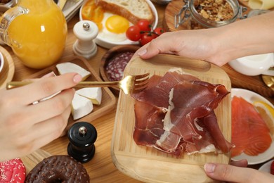 Photo of Women eating different food during brunch at wooden table, closeup