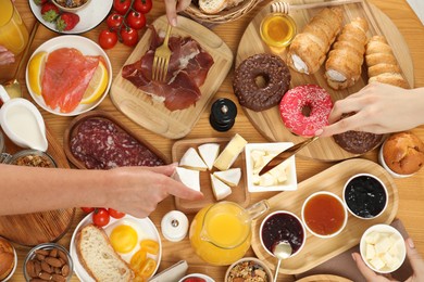 Photo of Women eating different food during brunch at wooden table, top view