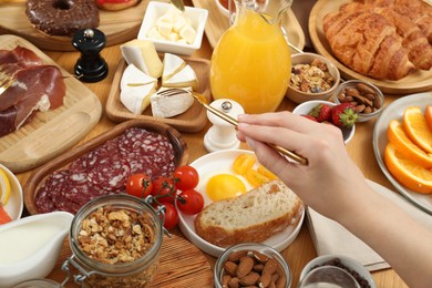 Photo of Woman eating different food during brunch at wooden table, closeup