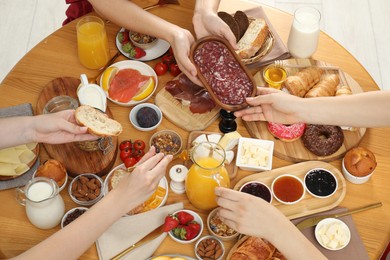 Photo of Women eating different food during brunch at wooden table, top view