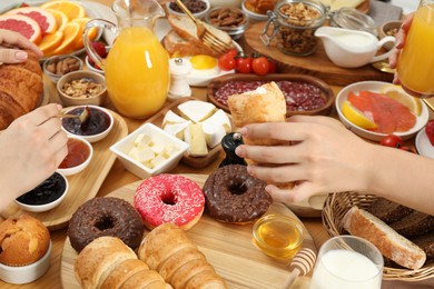 Photo of Women eating different food during brunch at wooden table, closeup