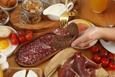 Photo of Woman eating different food during brunch at wooden table, closeup