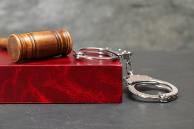 Book, judge's gavel and handcuffs on gray textured table, closeup