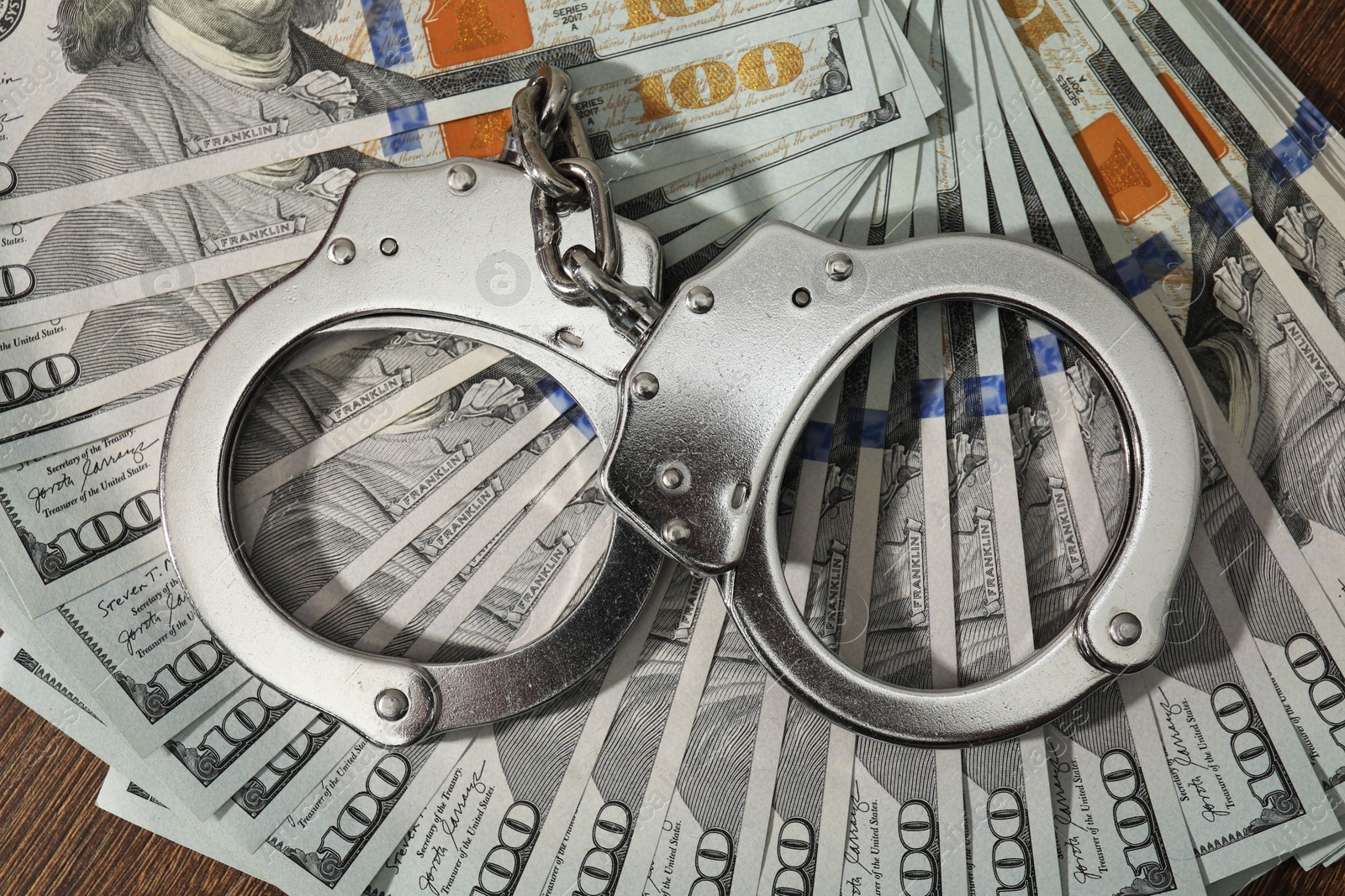 Photo of Handcuffs with dollar banknotes on wooden table, top view