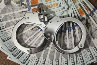 Photo of Handcuffs with dollar banknotes on wooden table, top view