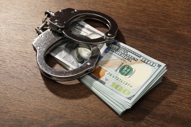 Photo of Handcuffs with dollar banknotes on wooden table