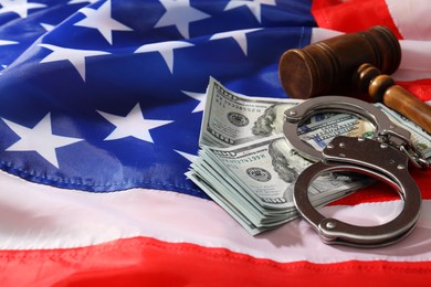 Photo of Handcuffs with dollar banknotes and wooden gavel on American flag, space for text