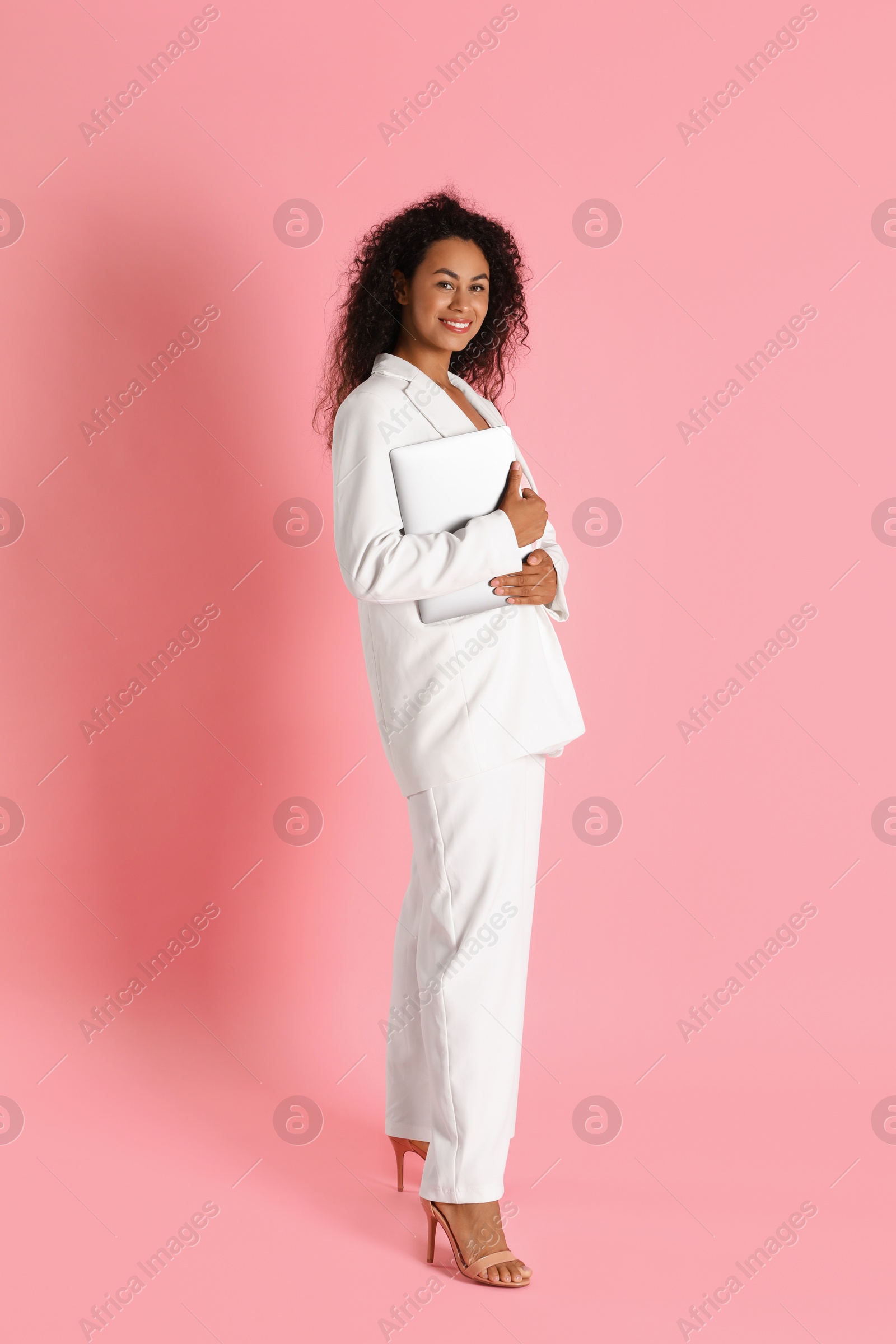 Photo of Beautiful woman in stylish suit with laptop on pink background