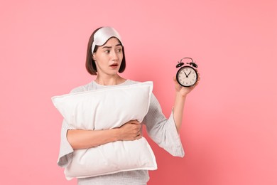 Photo of Overslept young woman with sleep mask, pillow and alarm clock on pink background