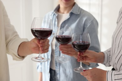 People clinking glasses of red wine indoors, closeup