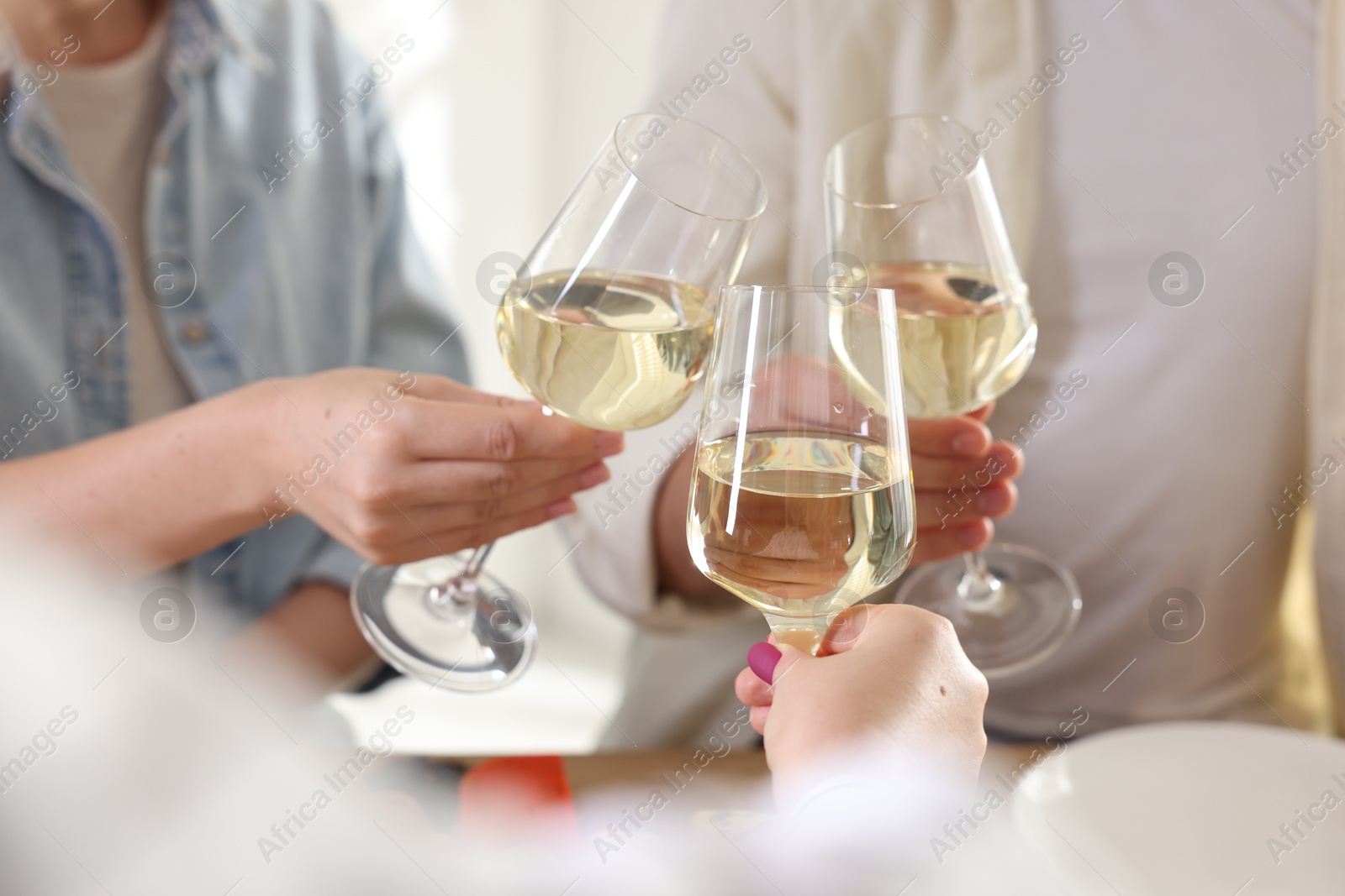 Photo of People clinking glasses of wine indoors, closeup