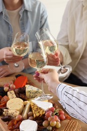 People clinking glasses of wine at served table, closeup