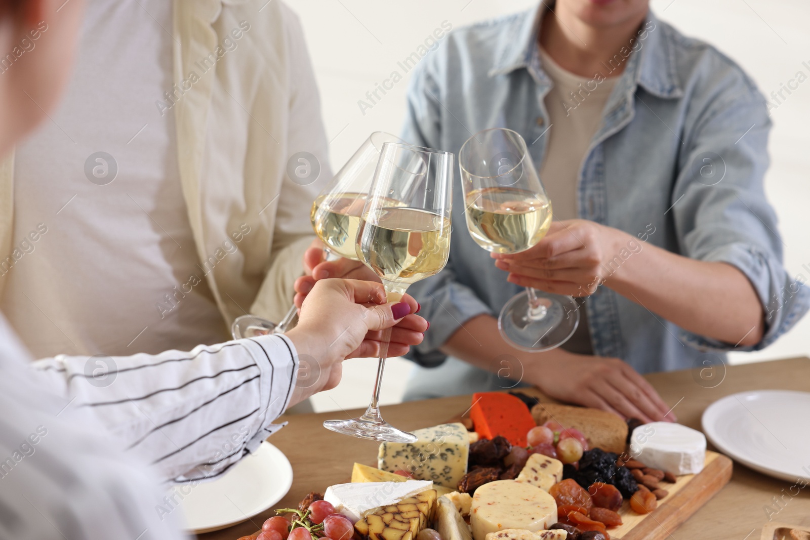 Photo of People clinking glasses of wine at served table, closeup