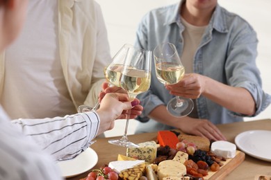 People clinking glasses of wine at served table, closeup