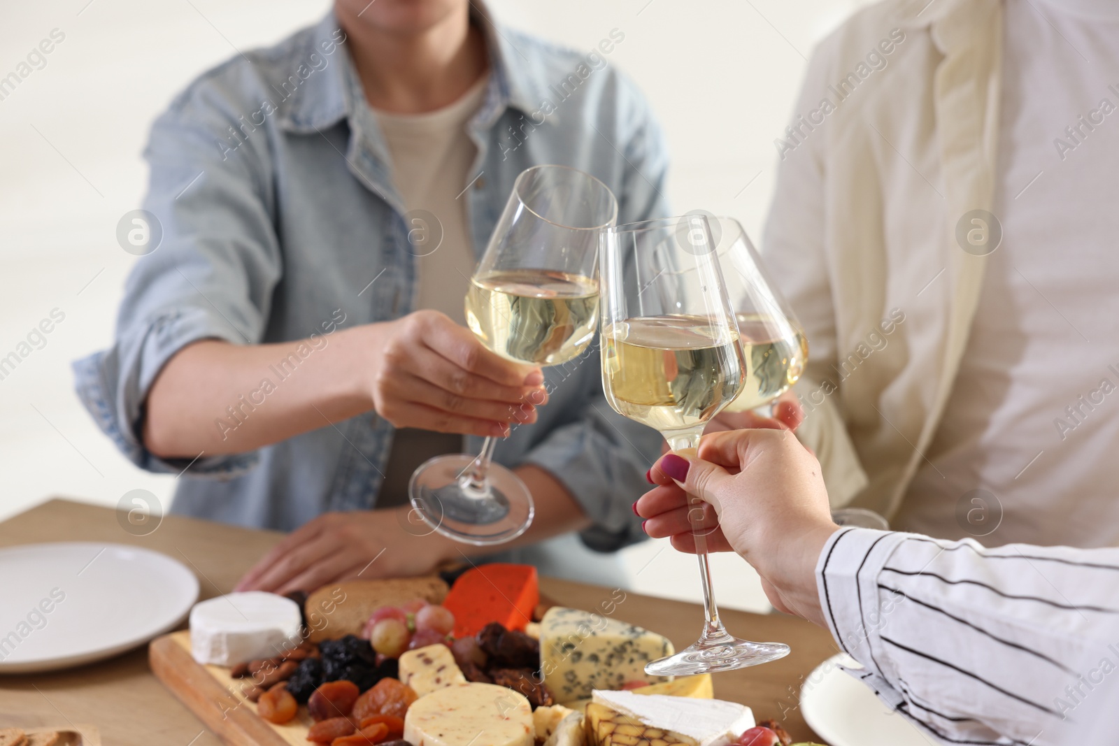 Photo of People clinking glasses of wine at served table, closeup