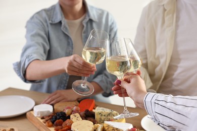 People clinking glasses of wine at served table, closeup