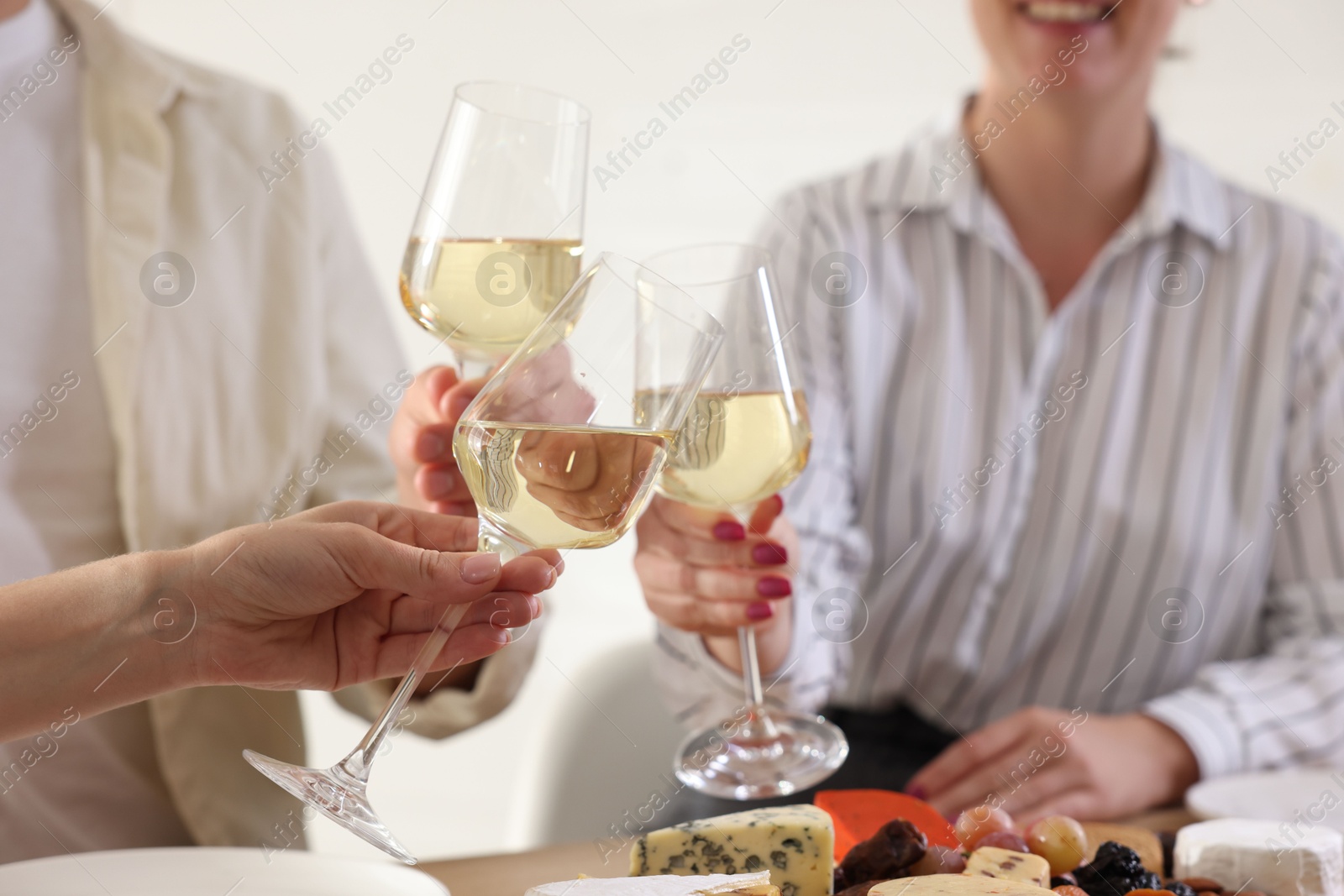 Photo of People clinking glasses of wine indoors, closeup