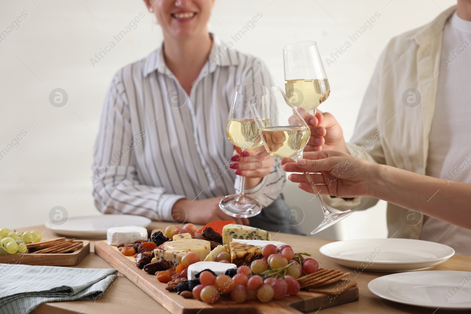 Photo of People clinking glasses of wine at served table, closeup