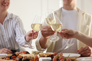 Photo of People clinking glasses of wine at served table, closeup