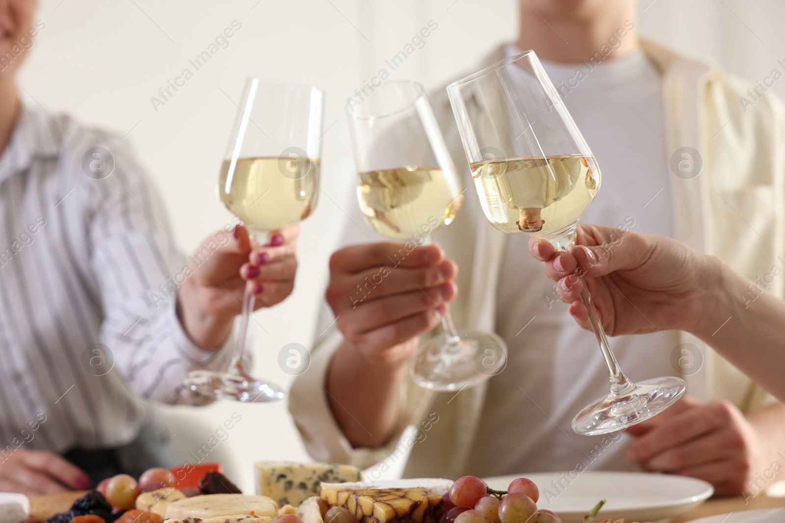 Photo of People clinking glasses of wine at served table, closeup