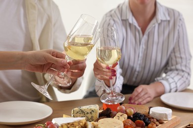 People clinking glasses of wine at served table, closeup