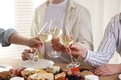 Photo of People clinking glasses of wine at served table, closeup