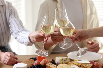 Photo of People clinking glasses of wine at served table, closeup