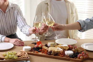 Photo of People clinking glasses of wine at served table, closeup