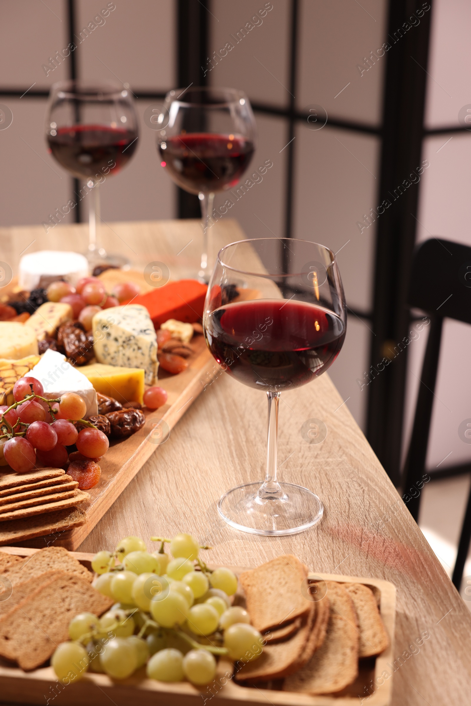 Photo of Glasses of red wine and different snacks on wooden table