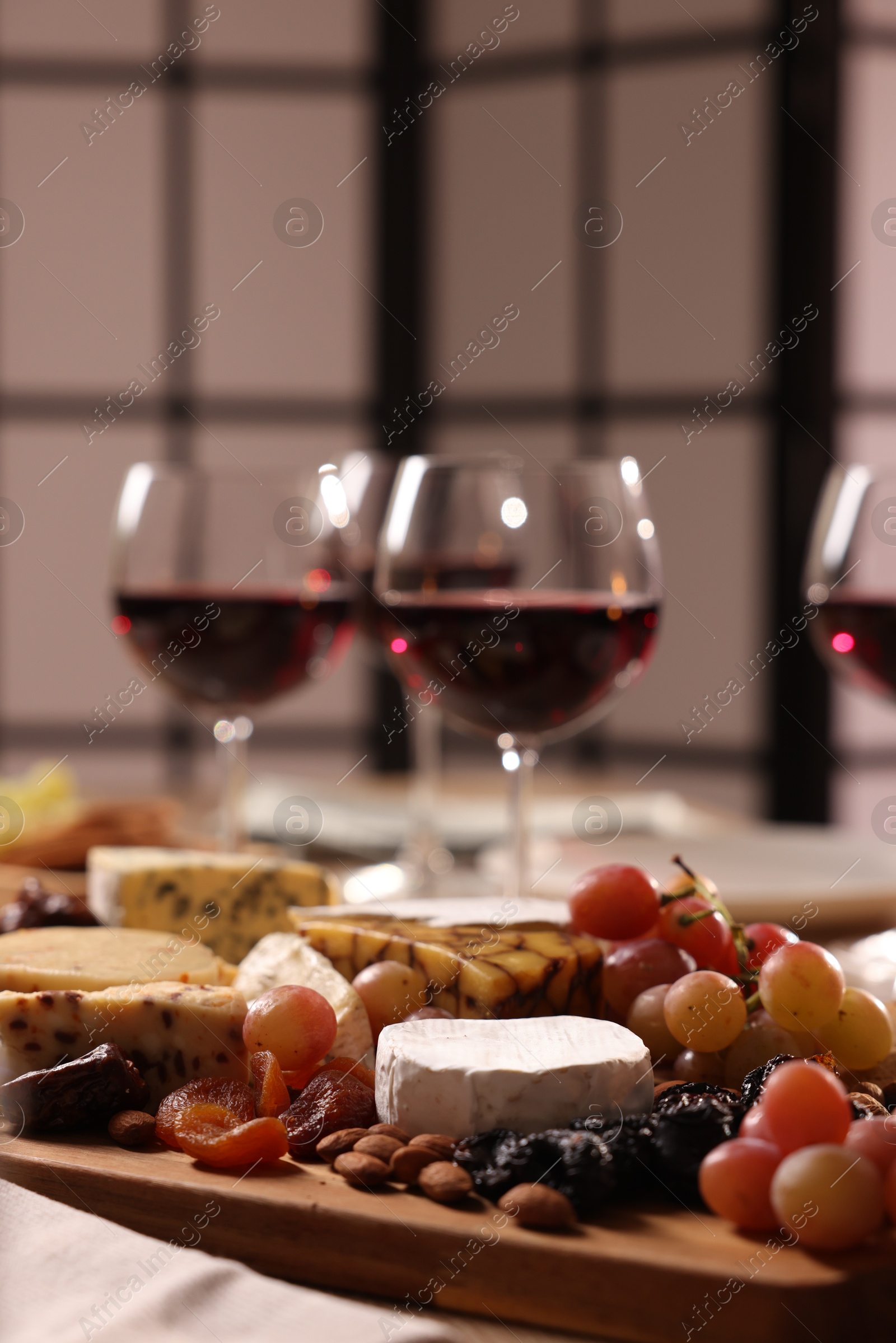 Photo of Glasses of red wine and different snacks on table, selective focus