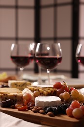 Photo of Glasses of red wine and different snacks on table, selective focus