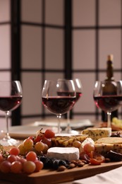 Photo of Glasses of red wine and different snacks on table, selective focus