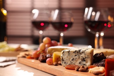 Photo of Glasses of red wine and different snacks on table, selective focus