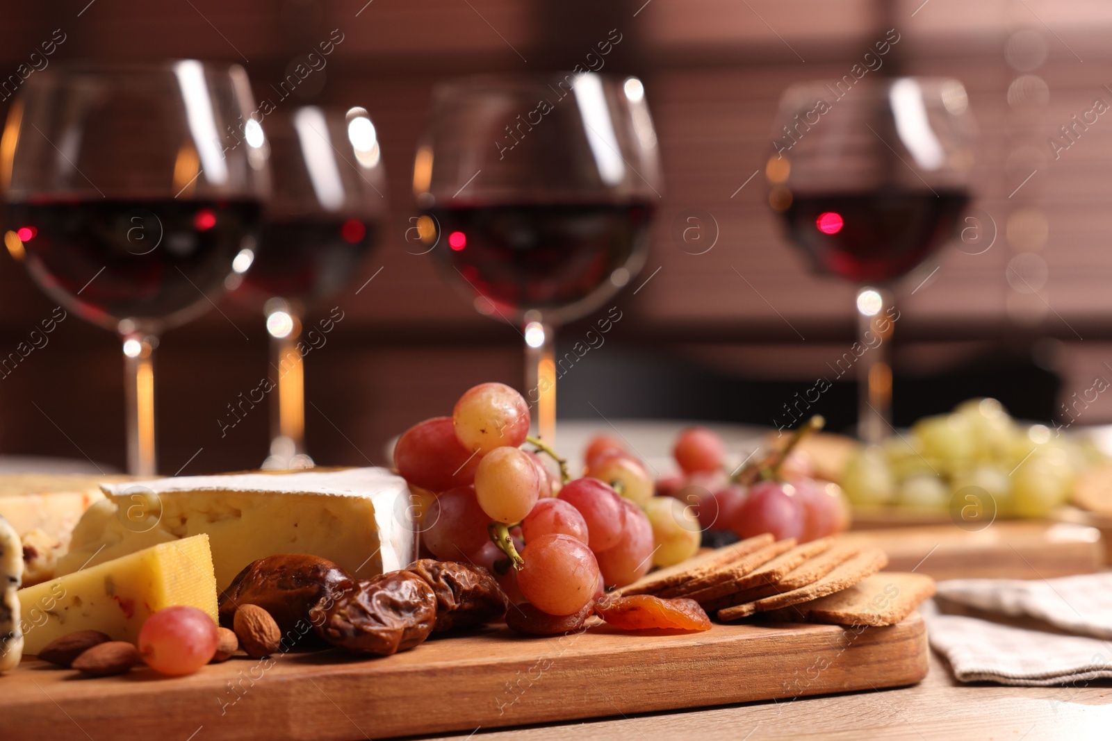 Photo of Glasses of red wine and different snacks on wooden table, selective focus