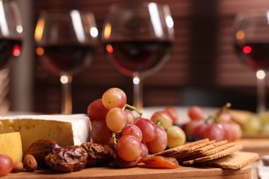 Photo of Glasses of red wine and different snacks on table, selective focus