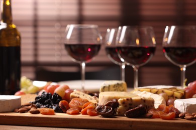 Photo of Glasses of red wine and different snacks on table, selective focus