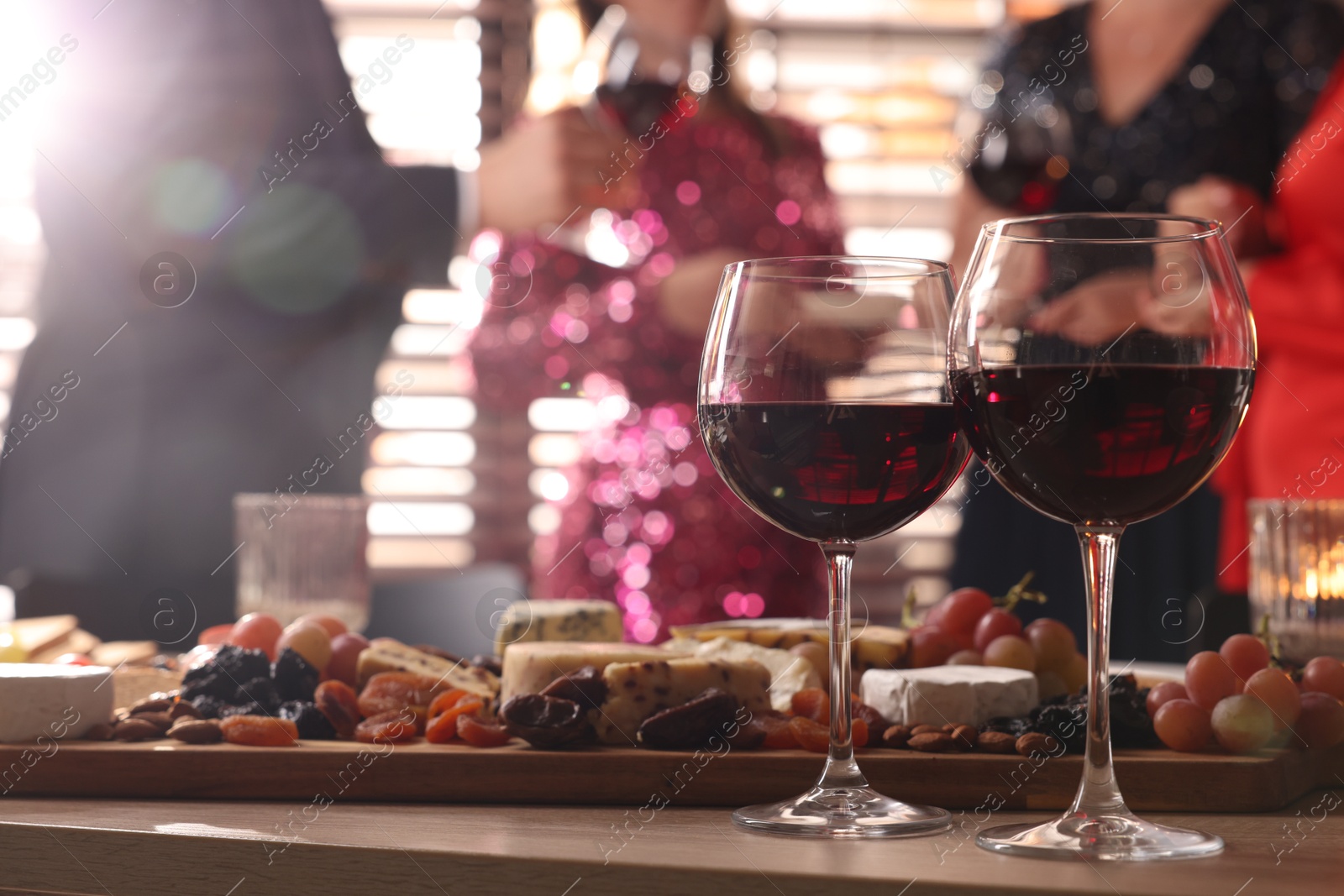 Photo of People holding glasses of wine at party, focus on wooden table with snacks and alcohol