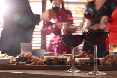 Photo of People holding glasses of wine at party, focus on wooden table with snacks and alcohol