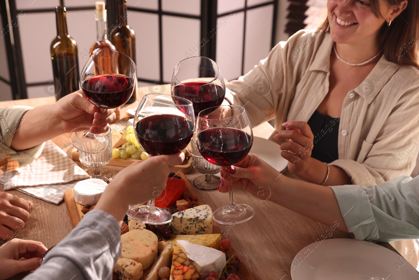 Photo of People clinking glasses of red wine at served table, closeup